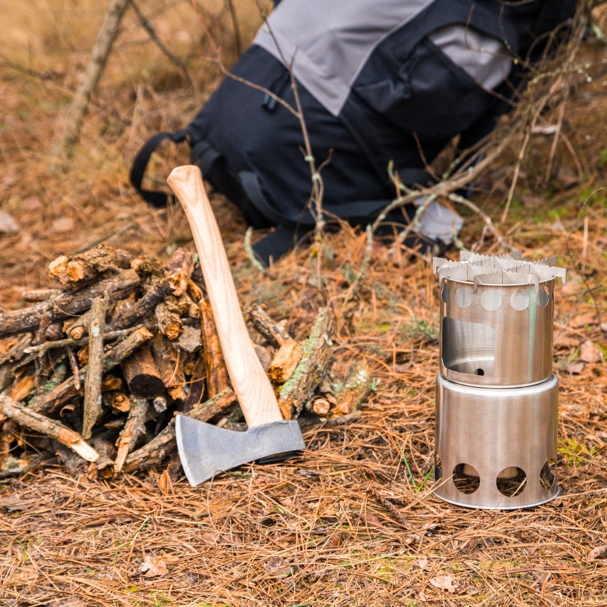 Bushcraft-Szene mit gestapeltem Feuerholz, Outdoor-Axt und kompakter Edelstahl-Feuerstelle – ideal für Survival, Trekking oder Waldcamping.