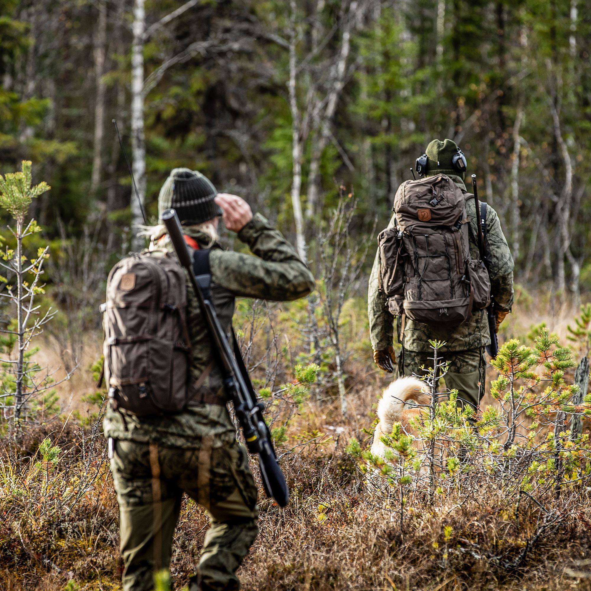 Jagd – zwei Jäger in Tarnkleidung mit Hunden und Rucksäcken im Wald
