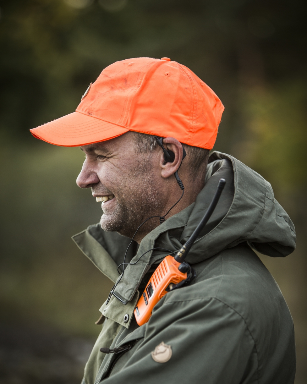 Jäger mit orangefarbener Signal-Kappe und Funkgerät im Wald – hochwertige Kopfbedeckung und Jagdzubehör für Sicherheit und Sichtbarkeit