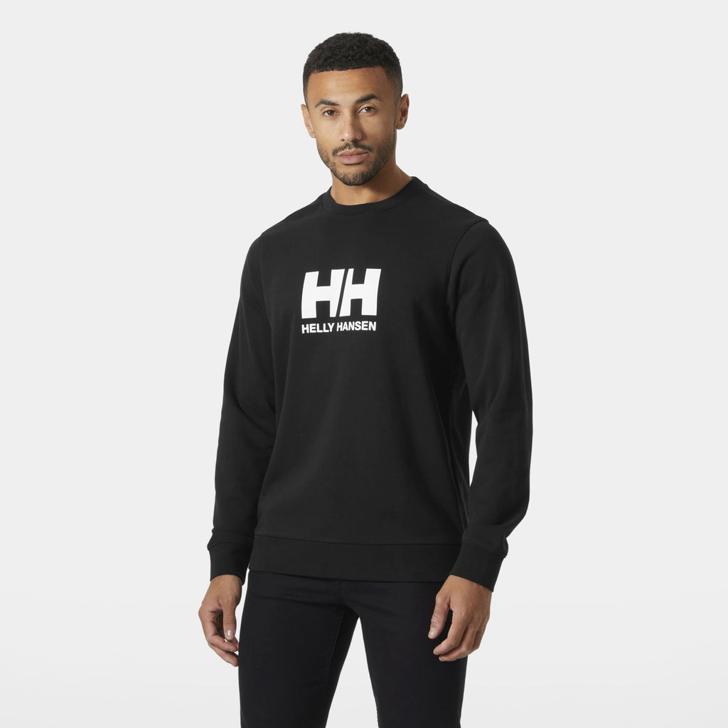 Mann trägt ein schwarzes Helly Hansen Sweatshirt mit weißem HH-Logo auf der Brust, steht vor neutralem Hintergrund und blickt leicht zur Seite