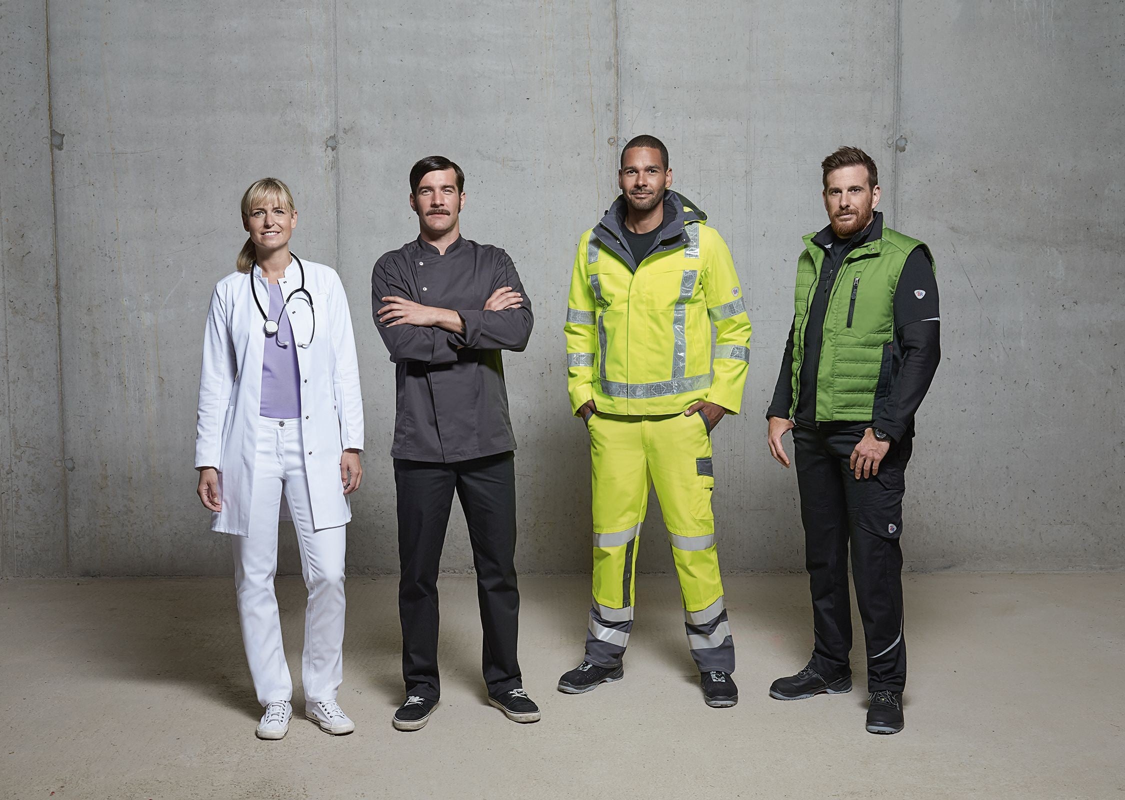 Vier Personen in Arbeitskleidung für Medizin, Gastronomie, Handwerk und Industrie vor grauer Betonwand – Symbolbild für vielseitigen Arbeitsbedarf bei GREWE.